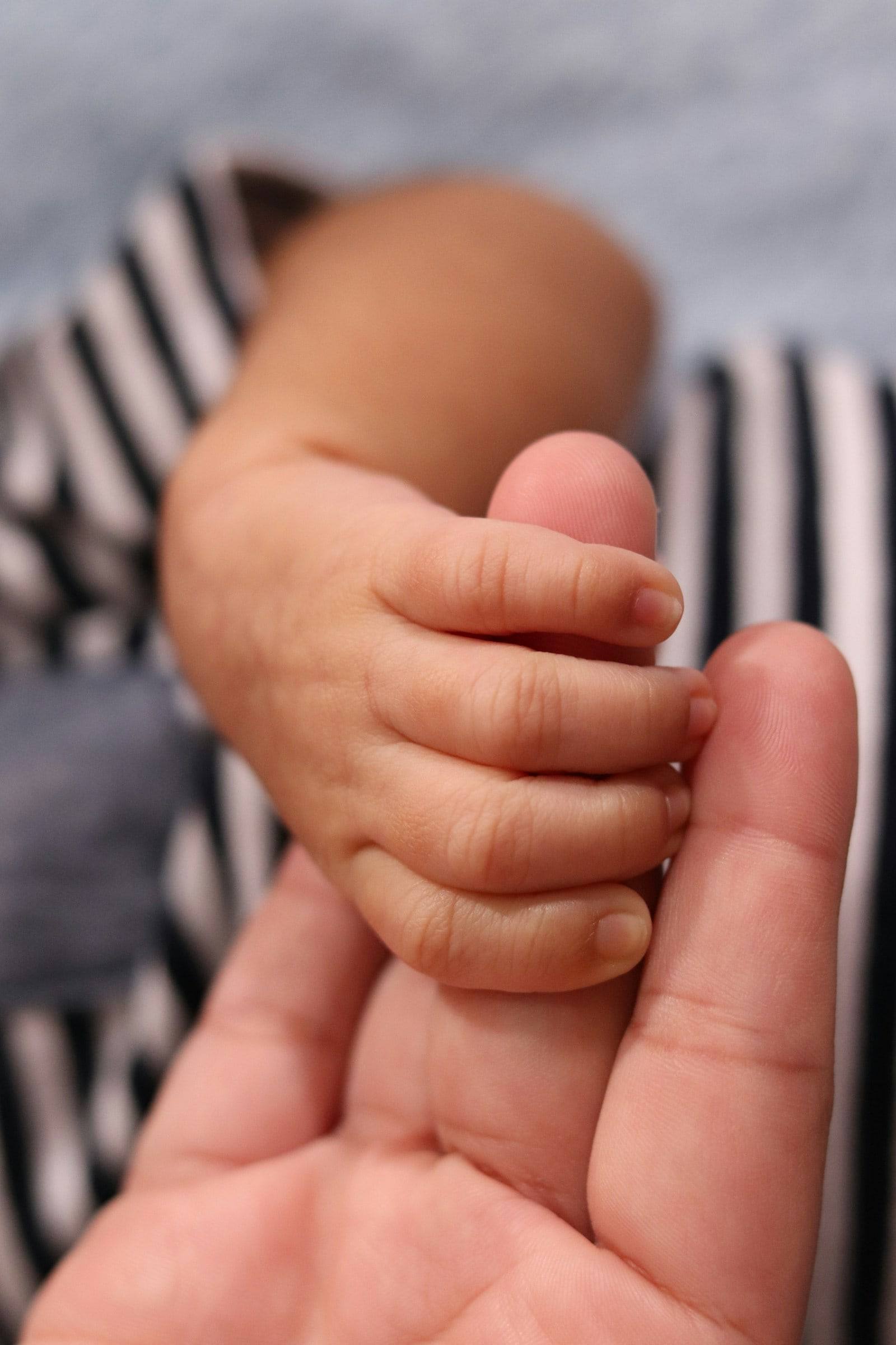 A baby’s tiny hand holding tight to an adult’s finger.