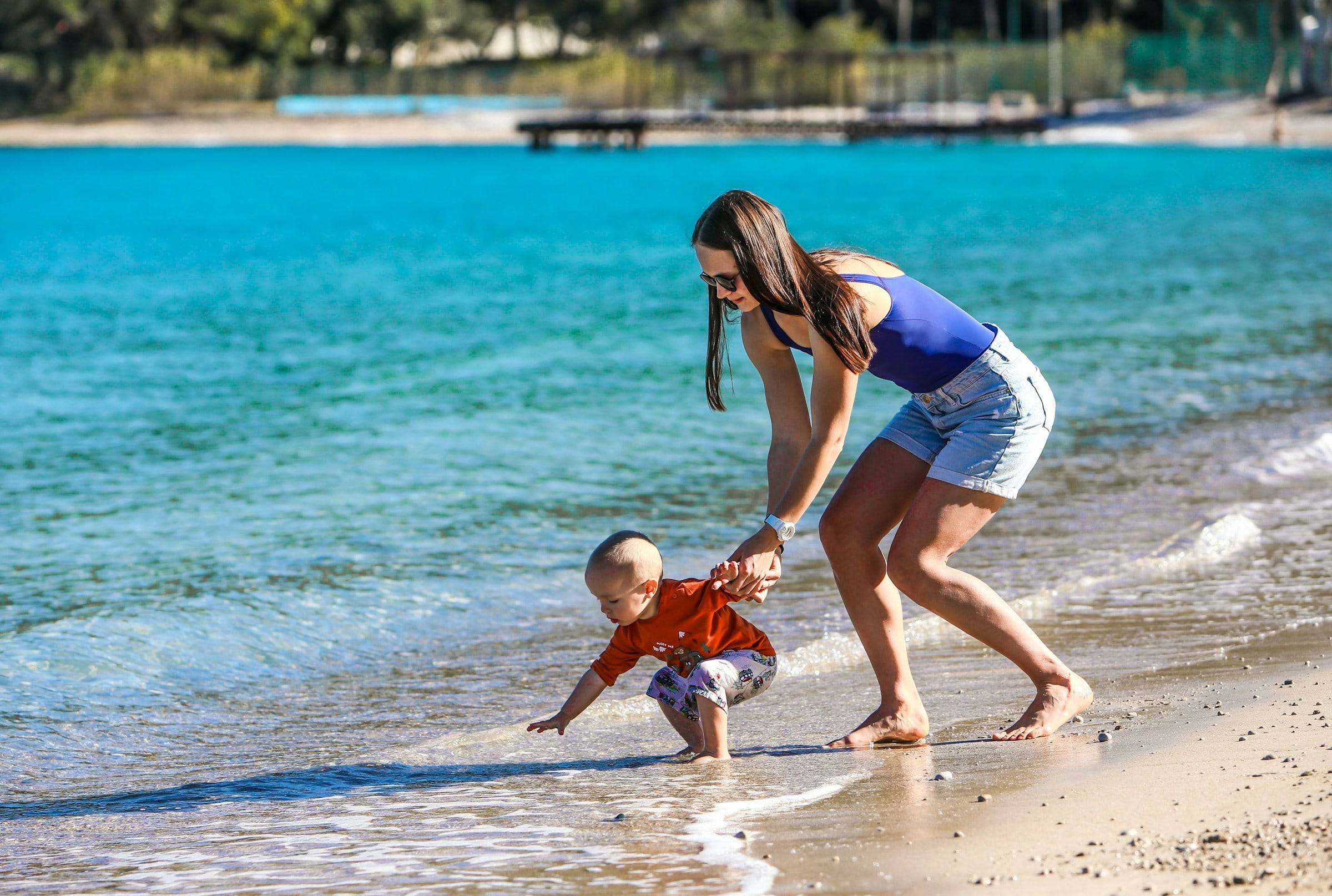 A mother walking her little boy by the hands into the sea.