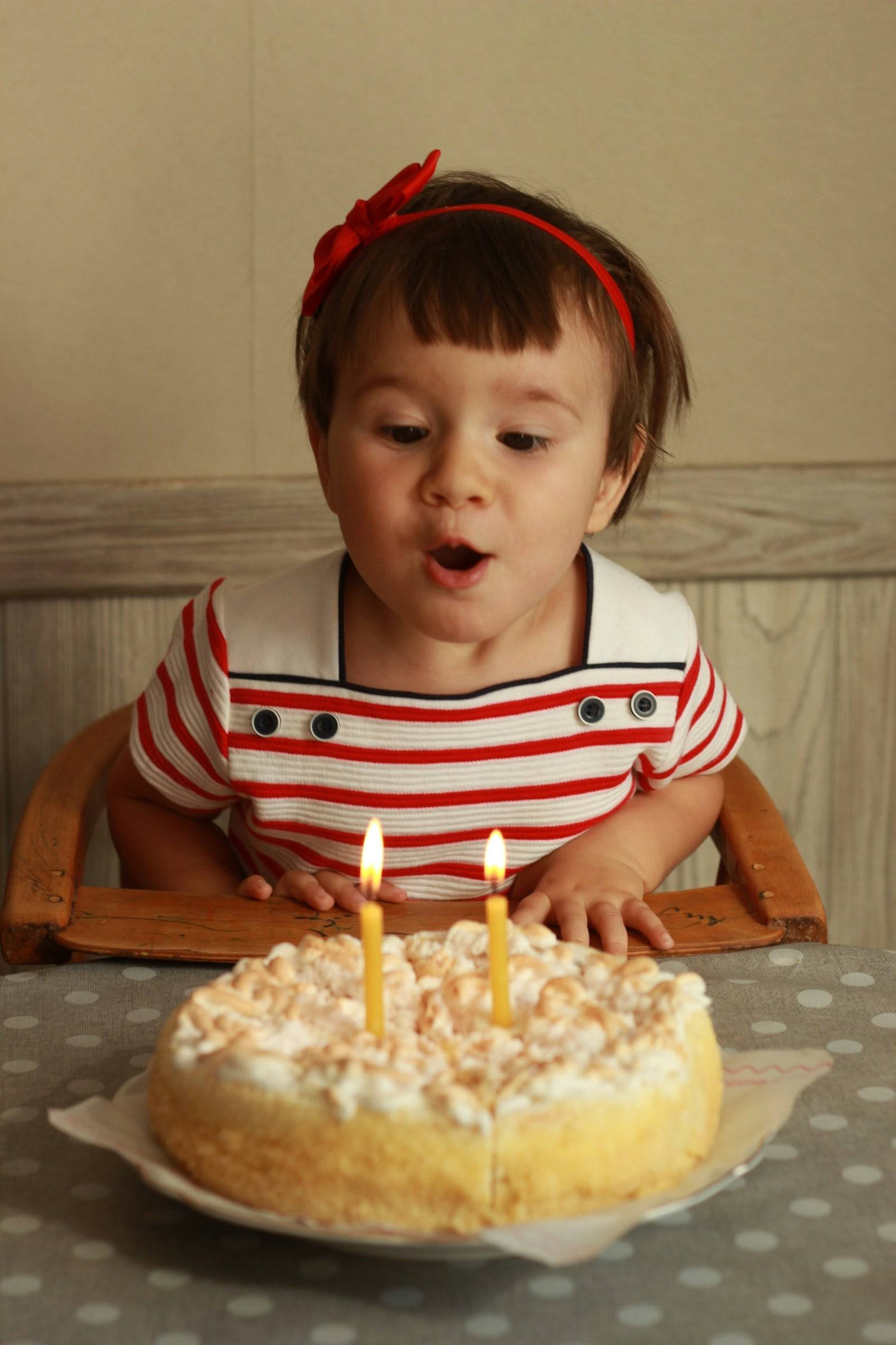 A small girl with a red bow blowing out the candles on her birthday cake.
