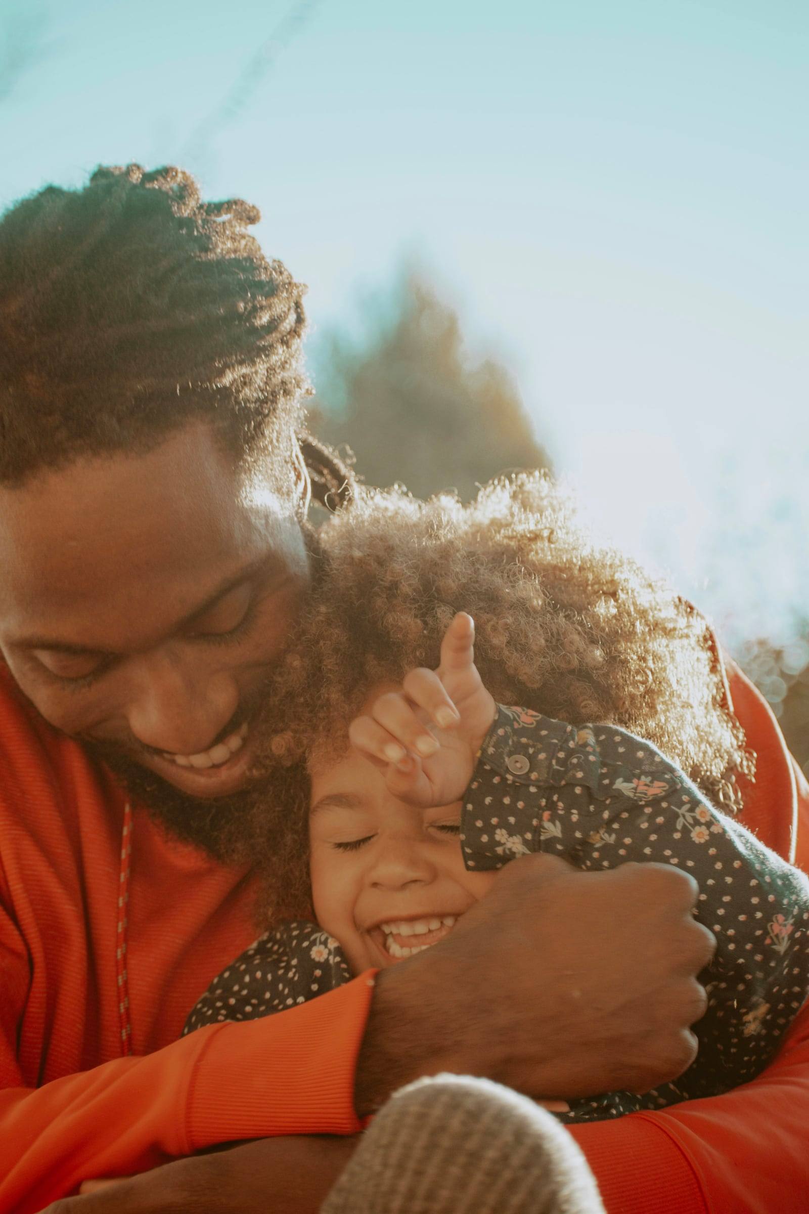 A father hugging his little daughter tight as she laughs in the sunlight.