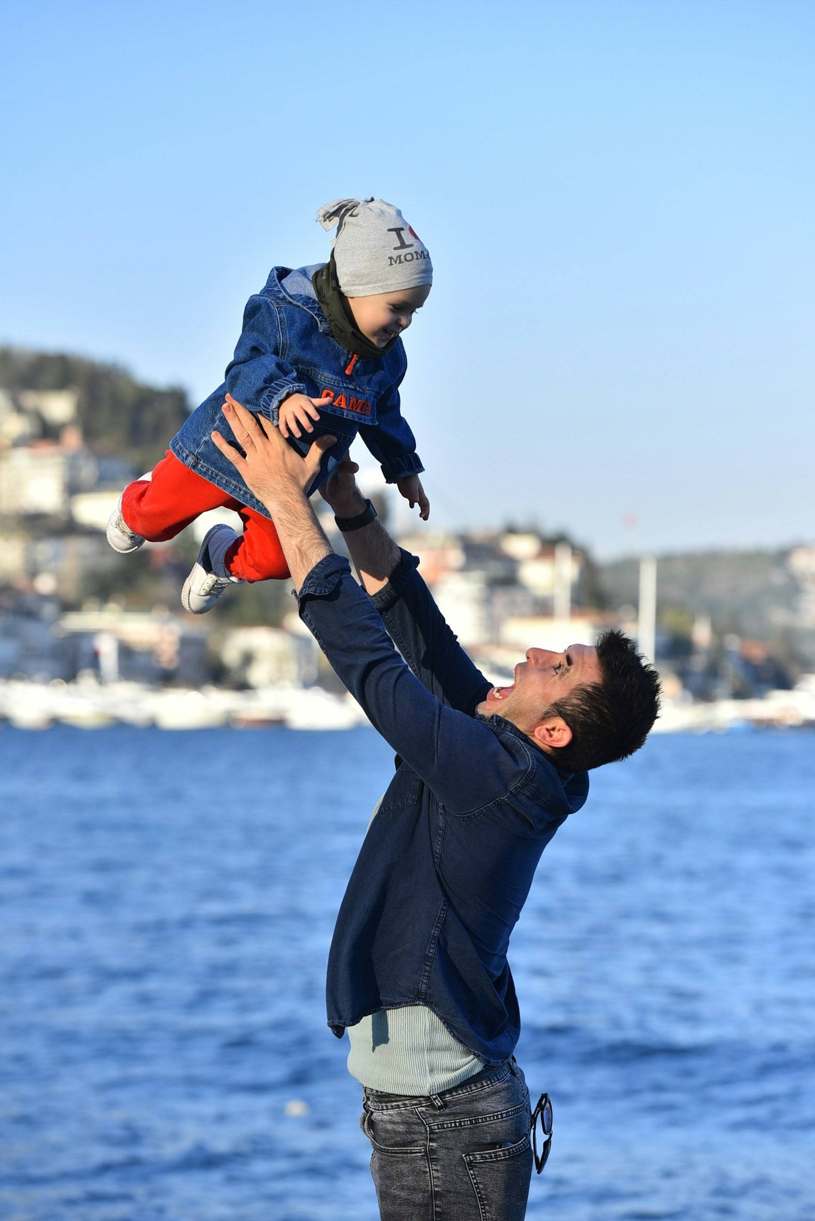 A father throwing his small child up into the air beside the Bosphorus.