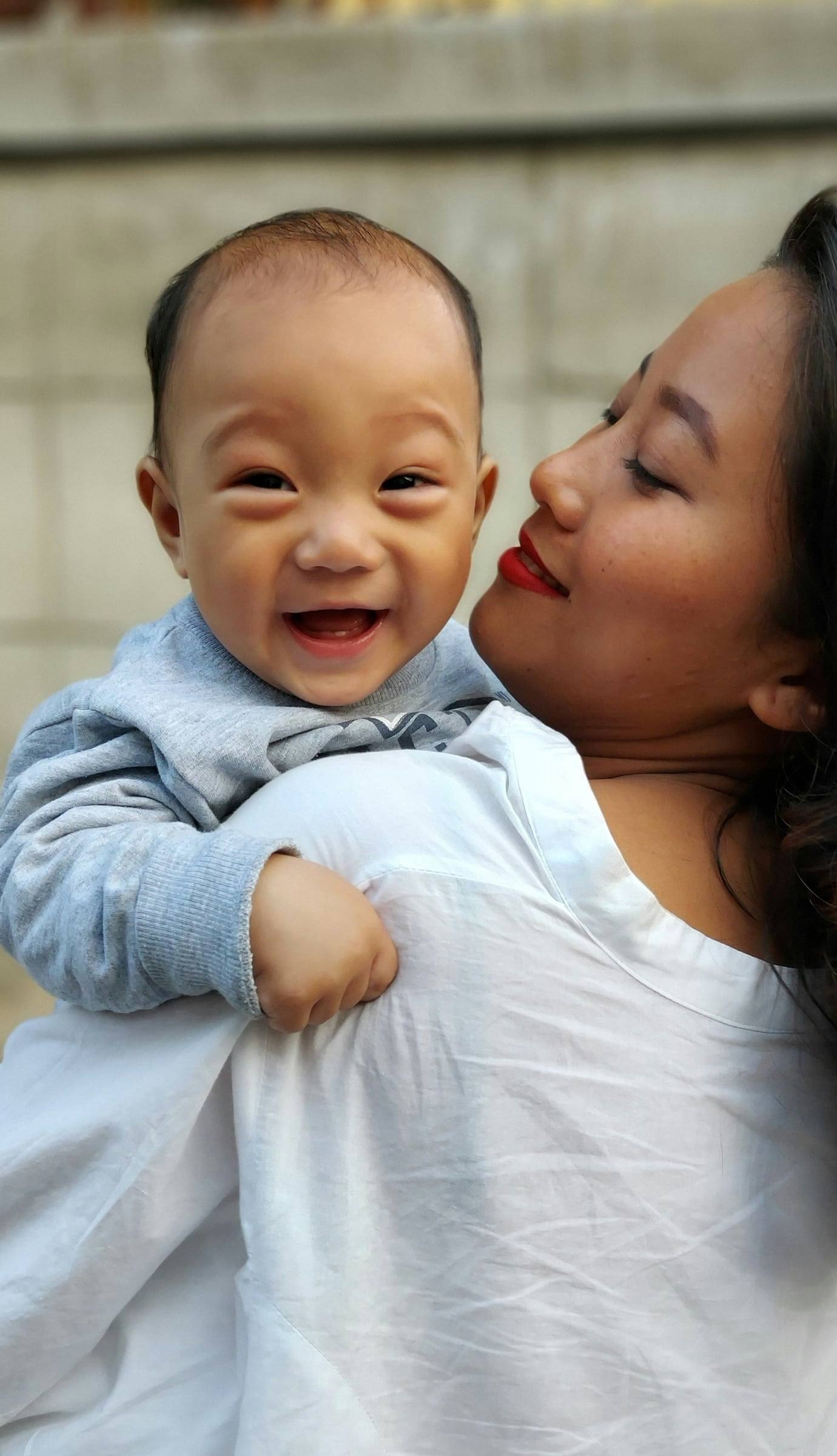 A baby laughing over their mother’s shoulder while she smiles with her eyes closed.