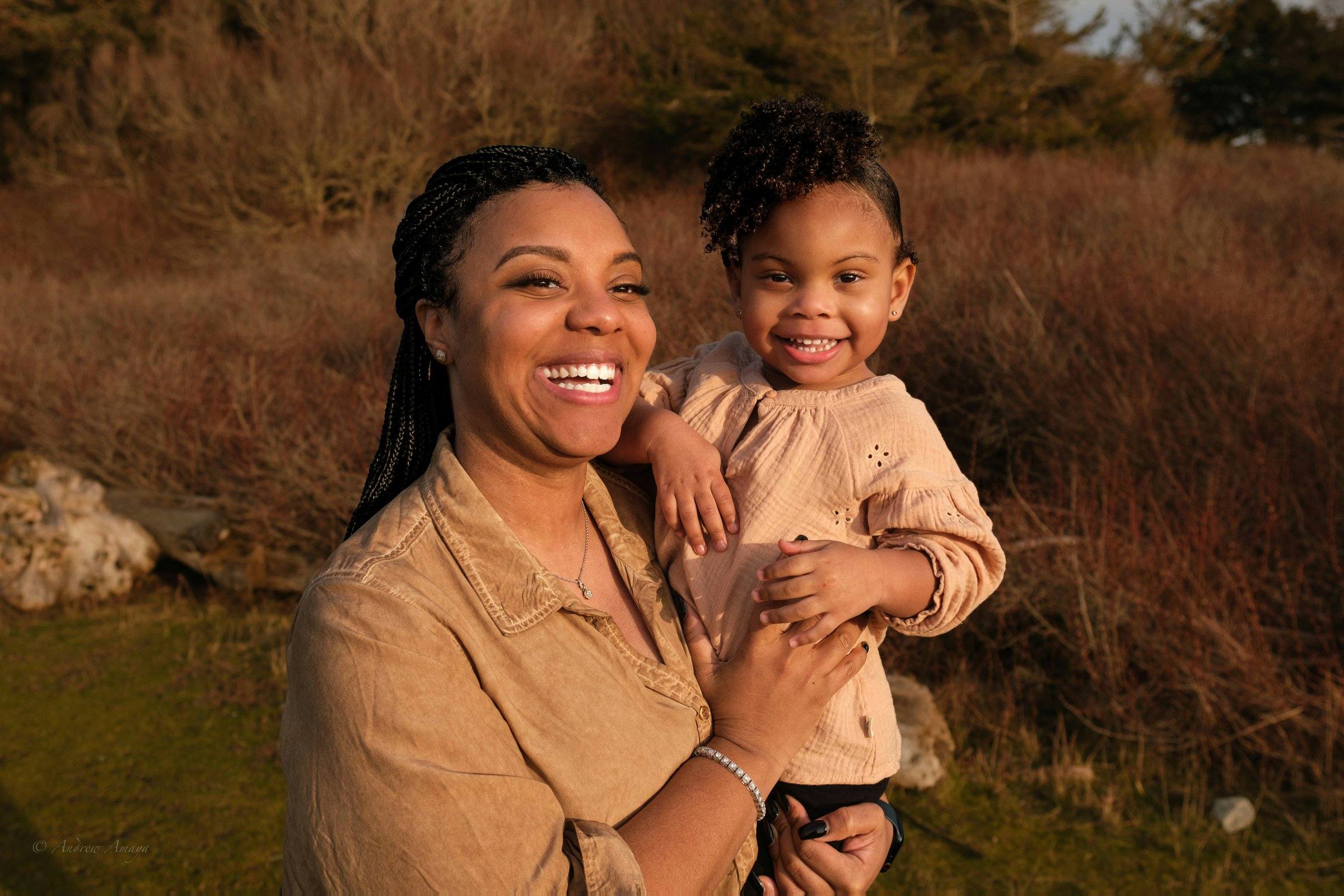 A mother laughing at sunset with her little daughter in her arms.