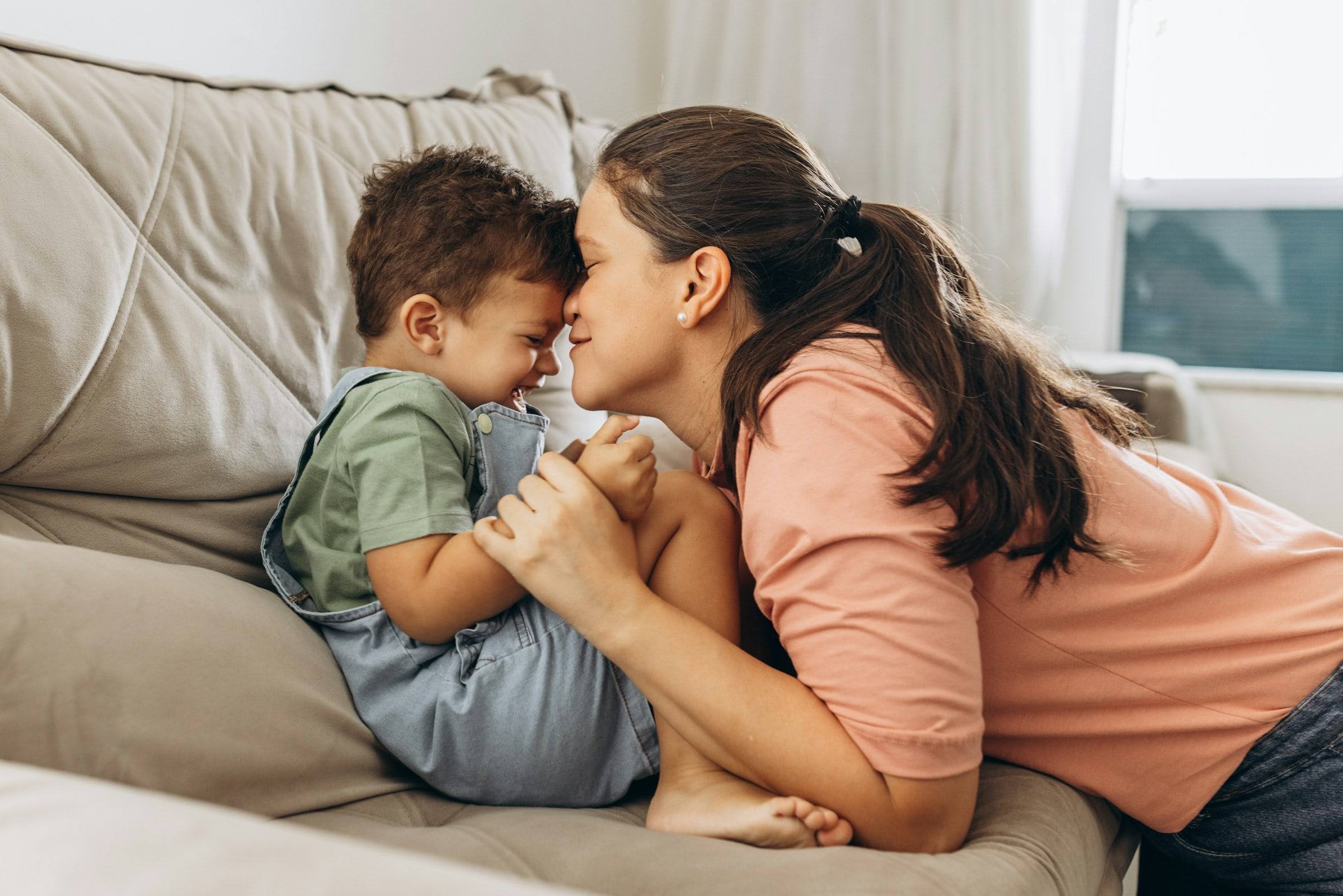 A mother and her little boy on the sofa, forehead to forehead, smiling.