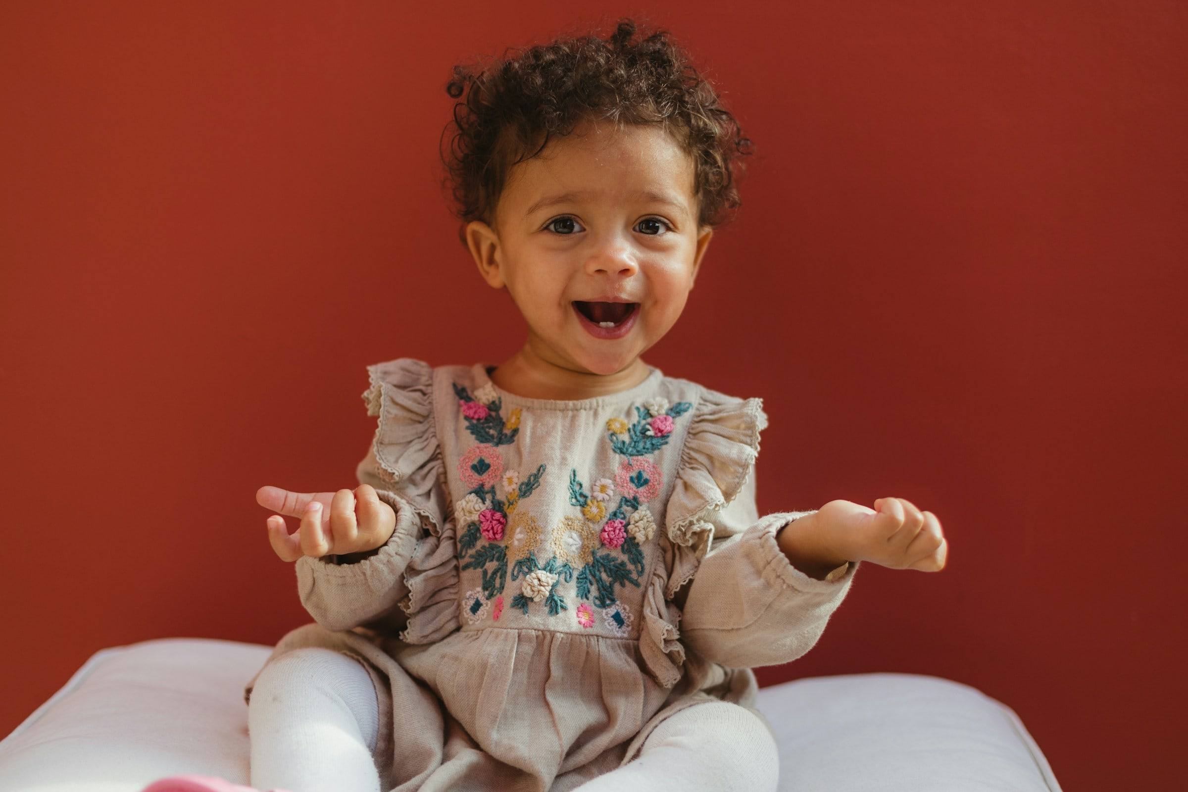 A curly-haired little girl laughing in front of a red wall.